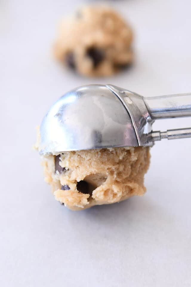 Cookie scoop scooping out chocolate chip cookie dough onto parchment paper.