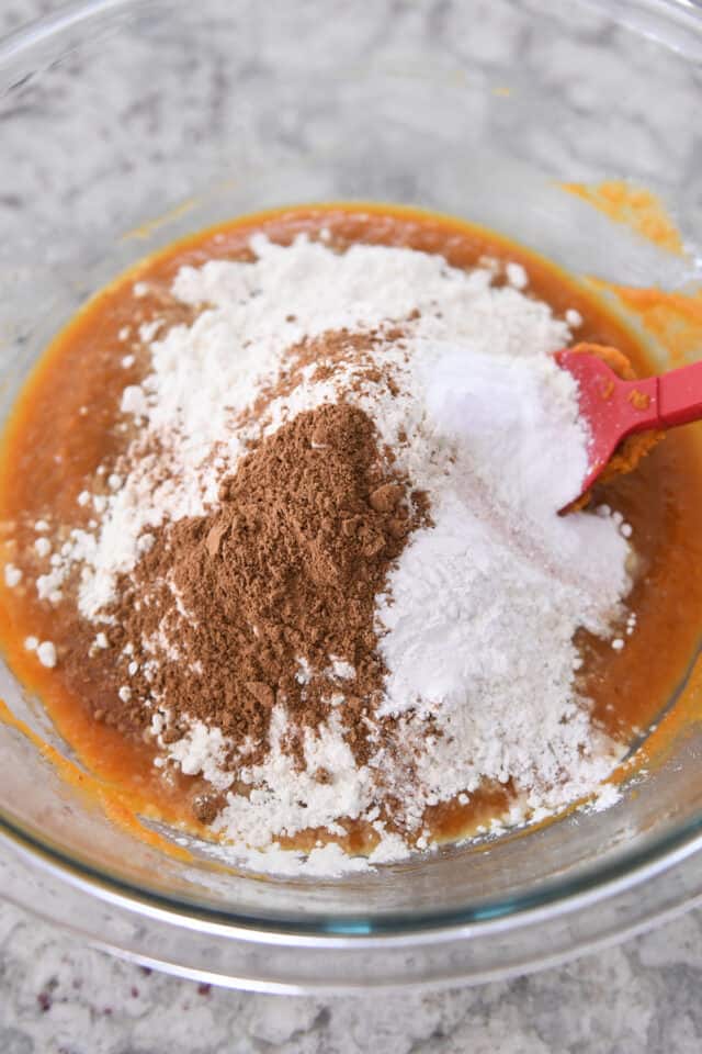 Cinnamon, flour, and baking soda in glass bowl with pumpkin batter.