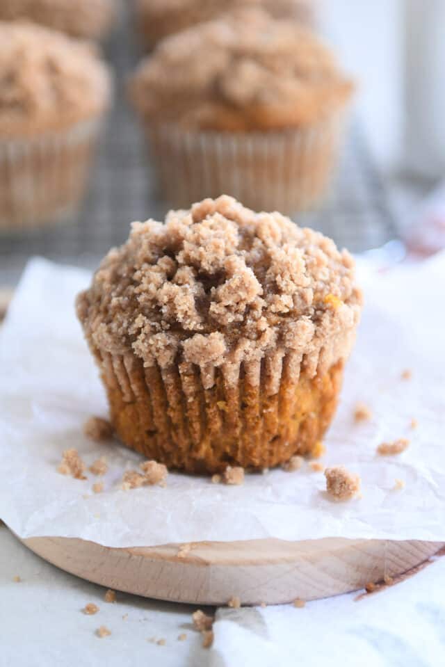 Streusel topped pumpkin muffin on white parchment paper with streusel crumbs.