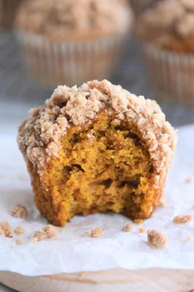 Pumpkin muffin with streusel on top and bite taken out on top of parchment paper.