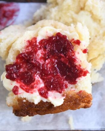 Raspberry jam and butter spread on half of a fluffy biscuit.