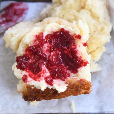 Raspberry jam and butter spread on half of a fluffy biscuit.