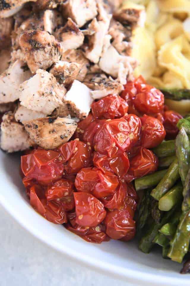 Roasted cherry tomatoes in white bowl next to grilled chicken.