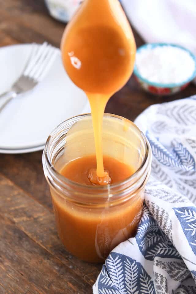 Wooden spoon drizzling caramel syrup into glass jar.