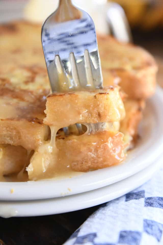 Fork piercing two pieces of French toast on white plate.