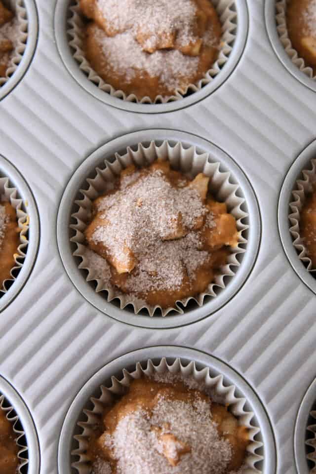 Pumpkin muffin batter in tins with cinnamon and sugar topping.