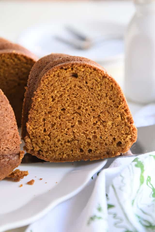 Slice of pumpkin bundt cake on server on white platter.