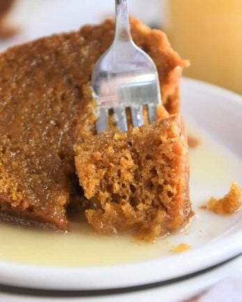 Bite of orange pumpkin cake being scooped out of big slice with fork on white plate.