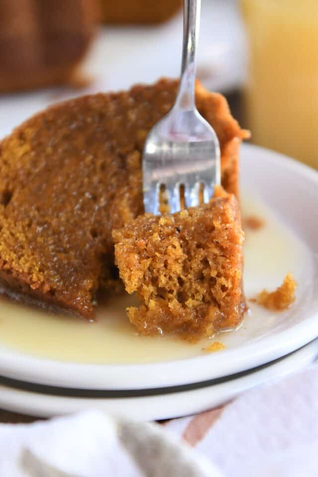 Bite of orange pumpkin cake on fork on white plate.