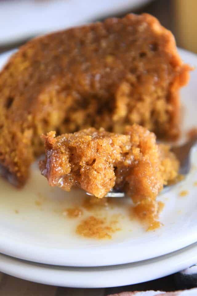 Bite of sauce-drenched cake on fork on white plate.