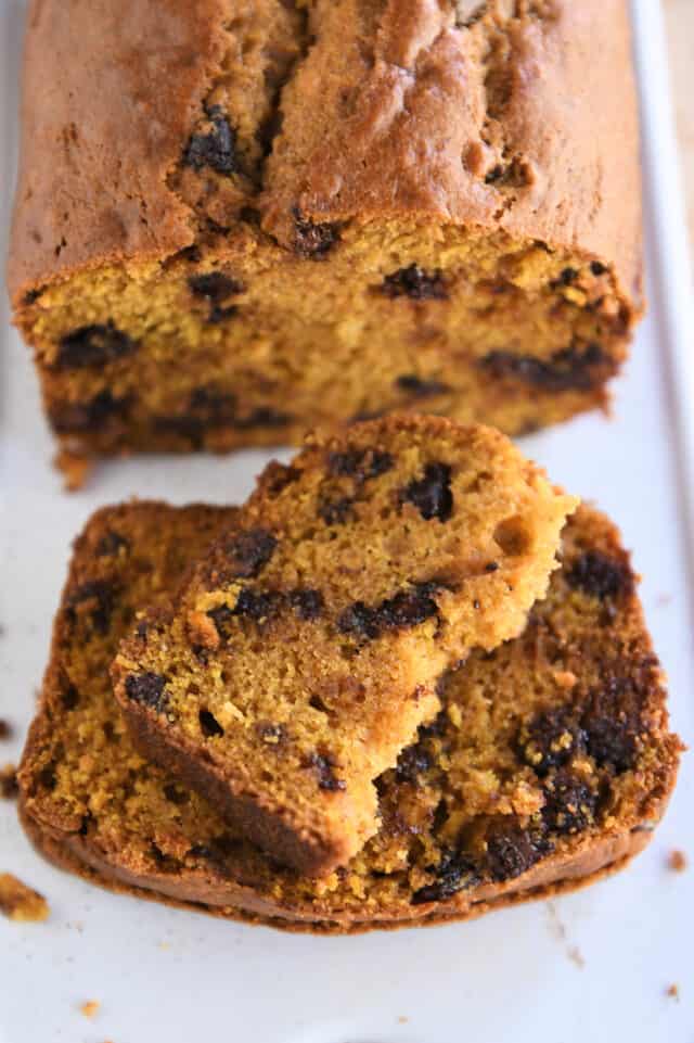 Half slice of pumpkin bread on top of two full slices on white platter.