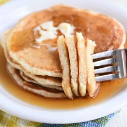 Four sourdough pancakes on white plate with fork piercing several pieces.