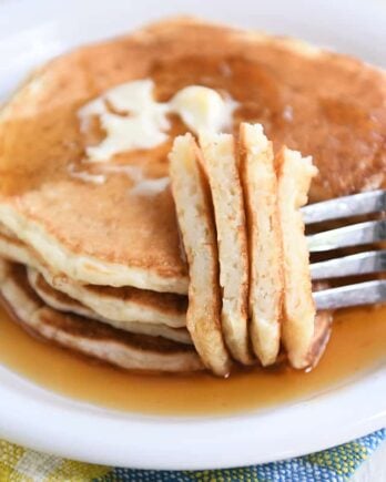 Four sourdough pancakes on white plate with fork piercing several pieces.