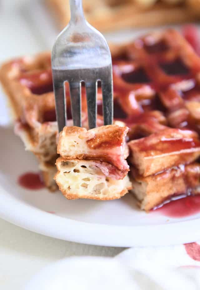 Fork with two pieces of waffle on white plate.