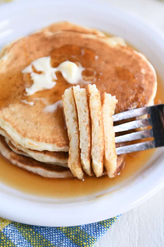 Four sourdough pancakes on white plate with fork piercing several pieces.