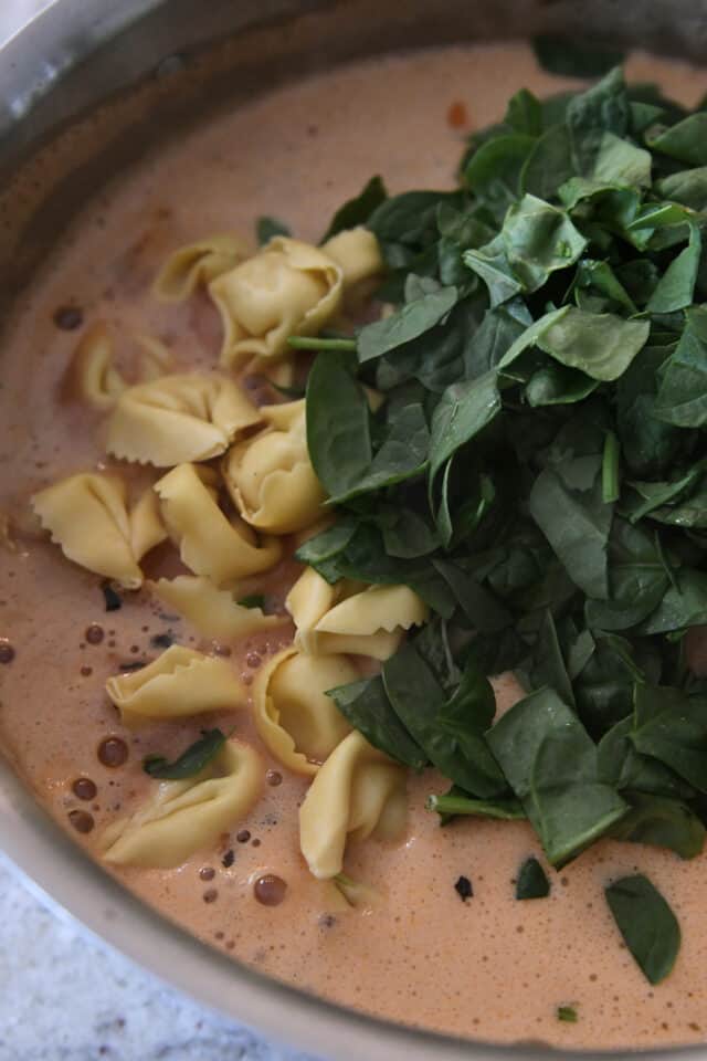 Tortellini and chopped spinach in pot with broth.