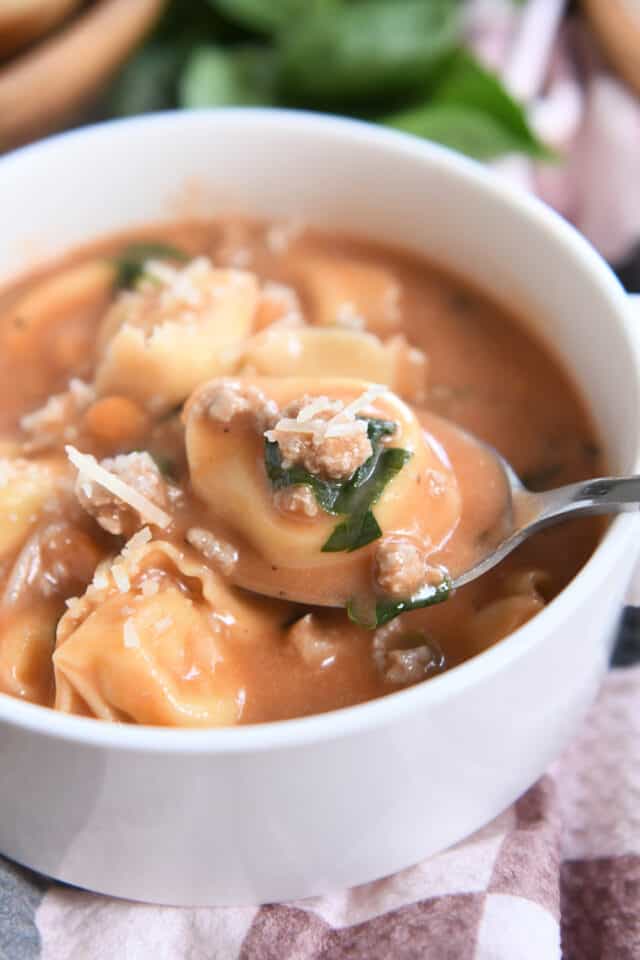 Spoonful of cheese tortellini, spinach and sausage in white bowl.