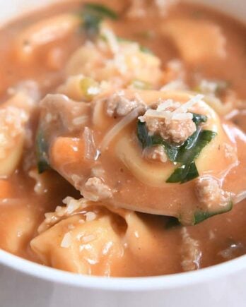 Spoonful of tortellini and creamy tomato broth in white bowl.