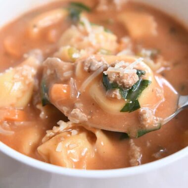 A spoonful of tortellini and creamy tomato soup in a white bowl.