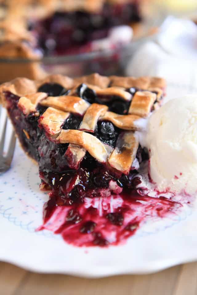 Bite removed from piece of triple berry pie on white plate with scoop of vanilla ice cream.