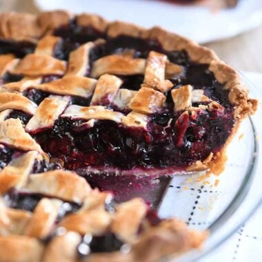 Triple berry pie in a glass pie plate with one piece removed.