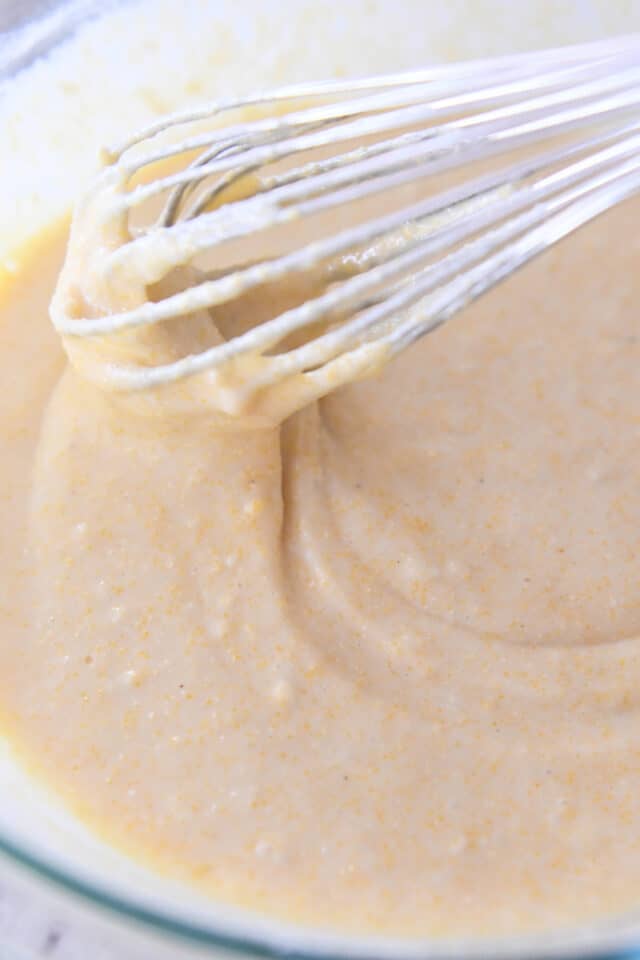 Whisk stirring cornbread batter in glass bowl.