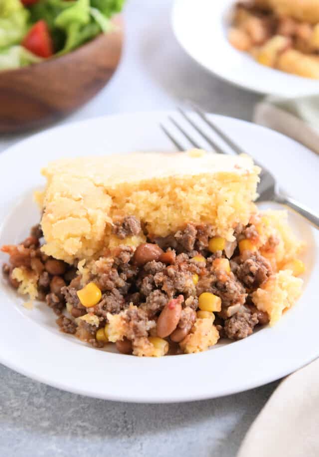 Cornbread topped beef, bean, and corn mixture on white plate with fork.