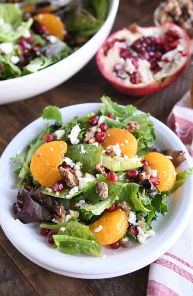 Salad greens, mandarin oranges, pomegranate arils, candied nuts and feta cheese on white plate.