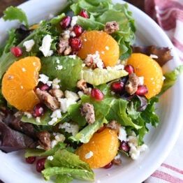 Salad greens, mandarin oranges, pomegranate arils, candied nuts and feta cheese on white plate.