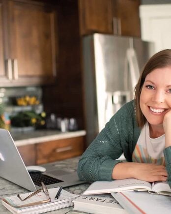 woman reading cookbooks at counter with laptop