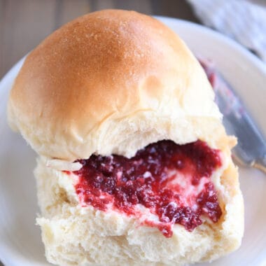 Soft dinner roll with butter and jam on white plate.
