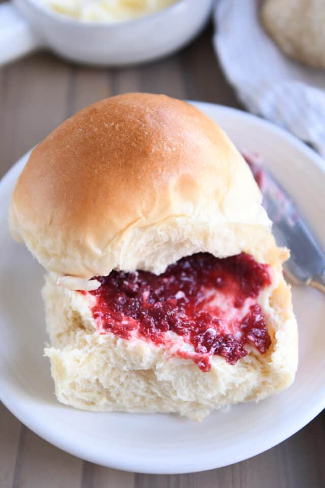 Soft dinner roll with butter and jam on white plate.