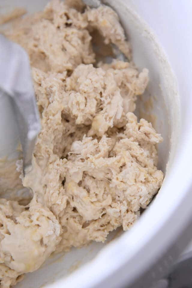 Shaggy mixture of roll dough in white bowl with dough hook.