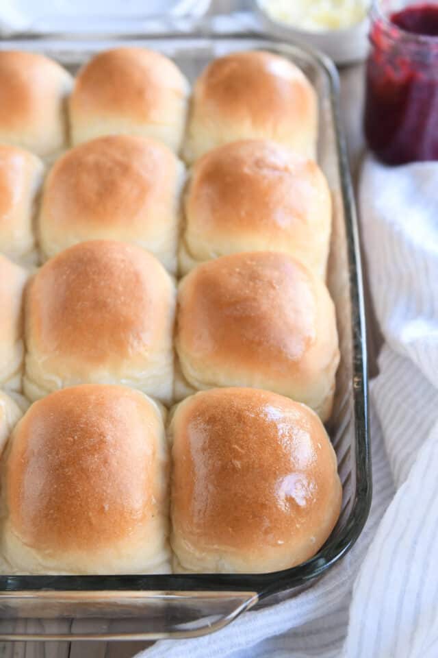 Twelve baked dinner rolls in glass pan with buttered tops.