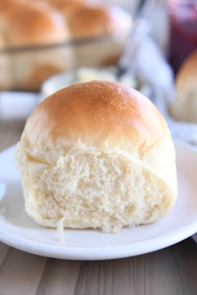 One soft and fluffy dinner roll on white plate.