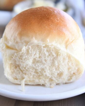 Baked soft and fluffy dinner roll on white plate.