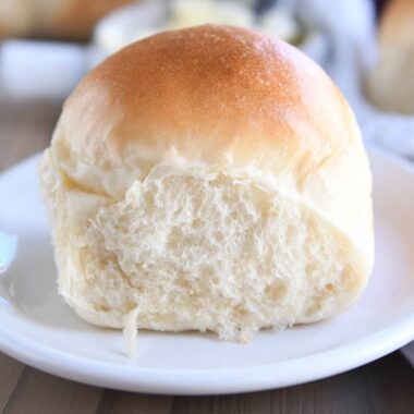 A fluffy dinner roll baked on a white plate.