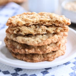 Four crispy oatmeal cookies stacked on white plate.