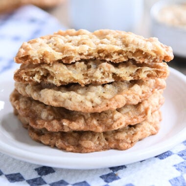 Four crispy oatmeal cookies stacked on white plate.