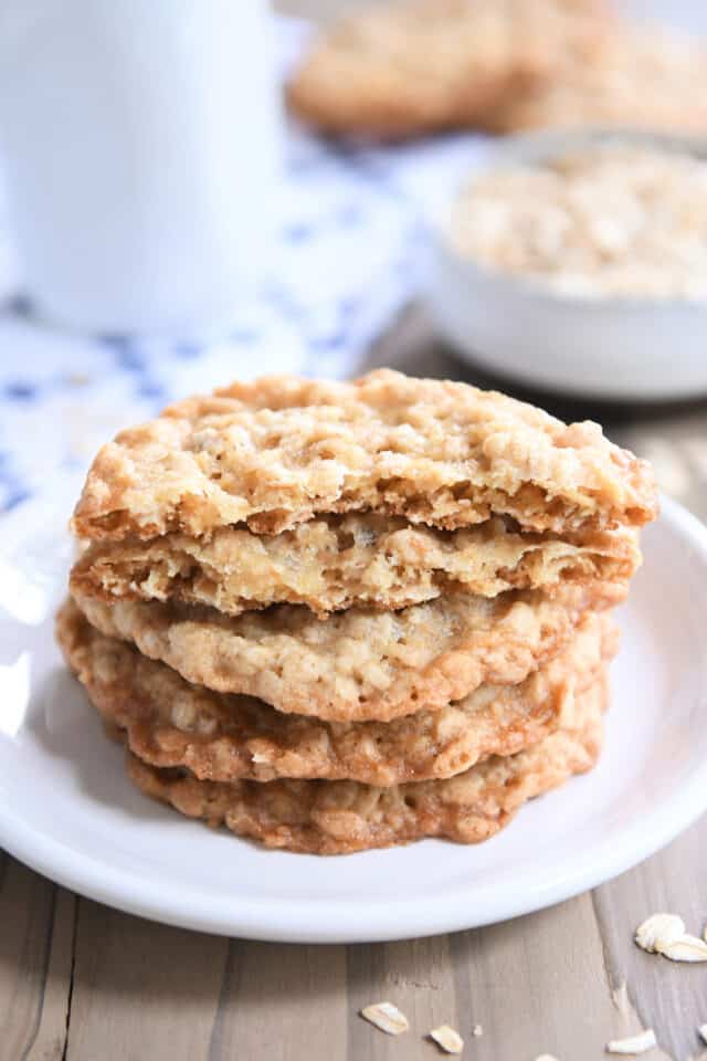 Four thin oatmeal cookies on white plate with top cookie broken in half.