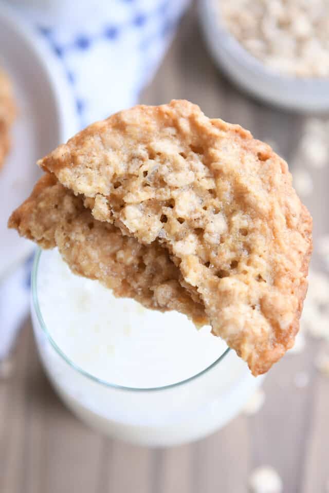 Two oatmeal cookie halves sitting on rim of glass of milk.