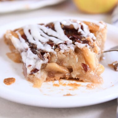 Slice of apple pie on white plate with one piece gone.