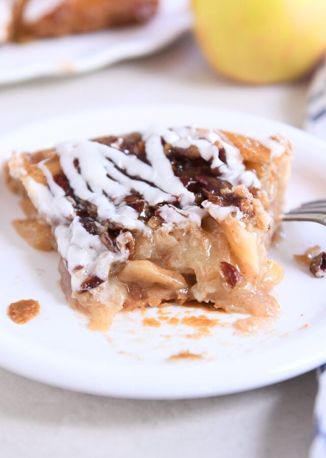 Piece of apple pie on white plate with one bite gone.