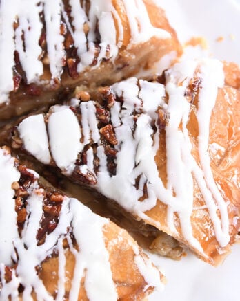 Slice of apple pie with pecans on top and drizzled with glaze.