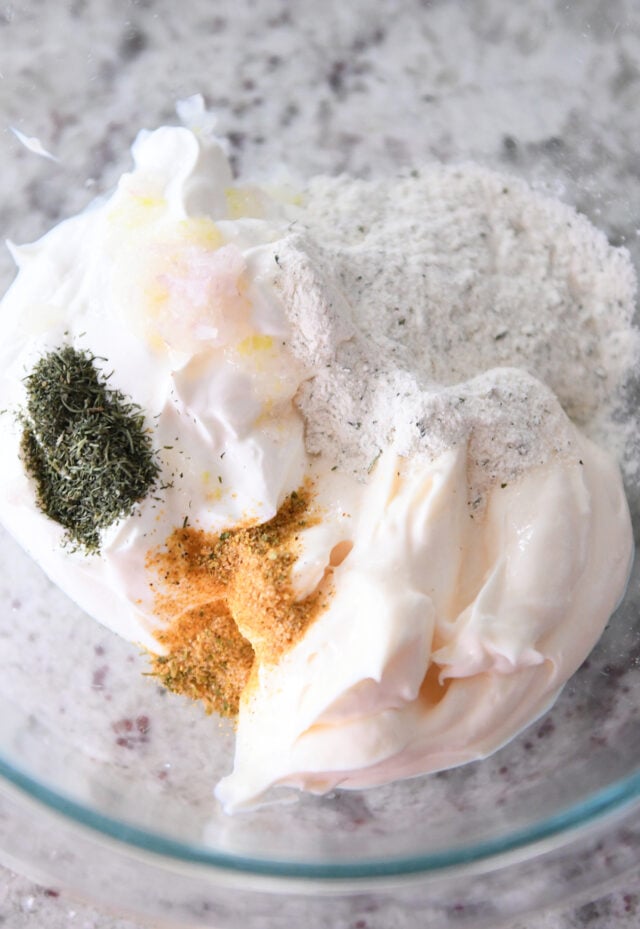 Glass bowl with mayonnaise, sour cream, spiced salt, ranch powder and dill.