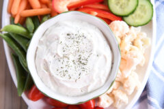 Veggie dip in small glass bowl surrounded by vegetables on white tray.