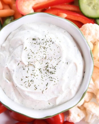 Veggie dip in small glass bowl surrounded by vegetables on white tray.