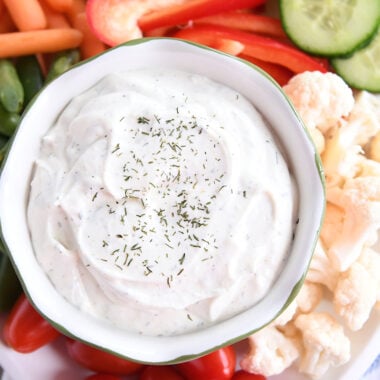 Veggie dip in small glass bowl surrounded by vegetables on white tray.