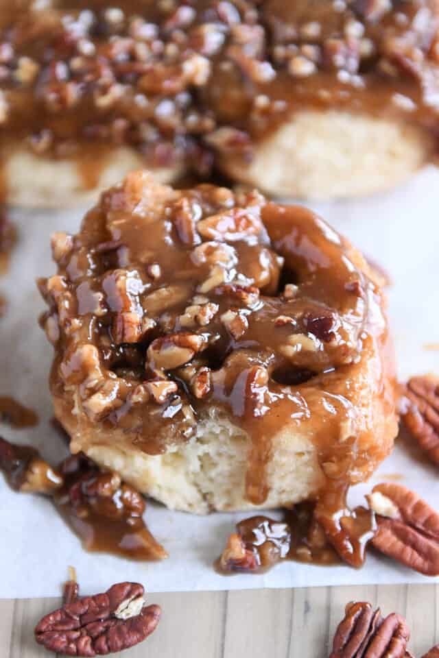 Caramel dripping down sides of sticky bun on white parchment paper.