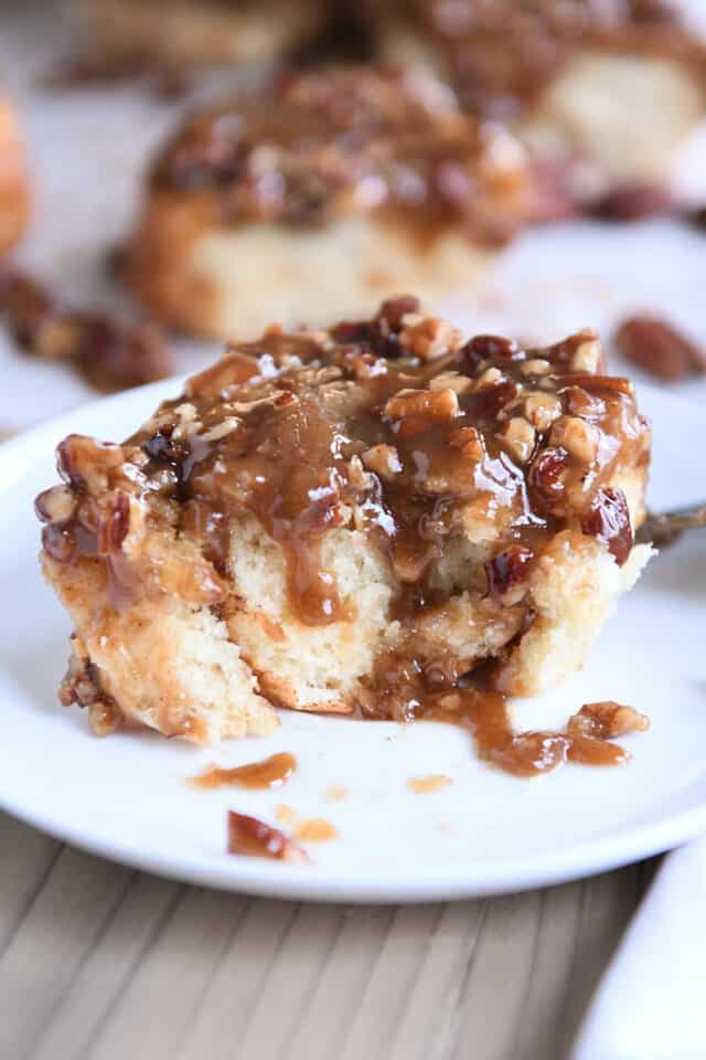 Half eaten caramel pecan sticky bun on white plate.